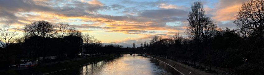 Sunset over the River Ouse, York. Blue sky with clouds and orange and grey streaks reflected in the water.