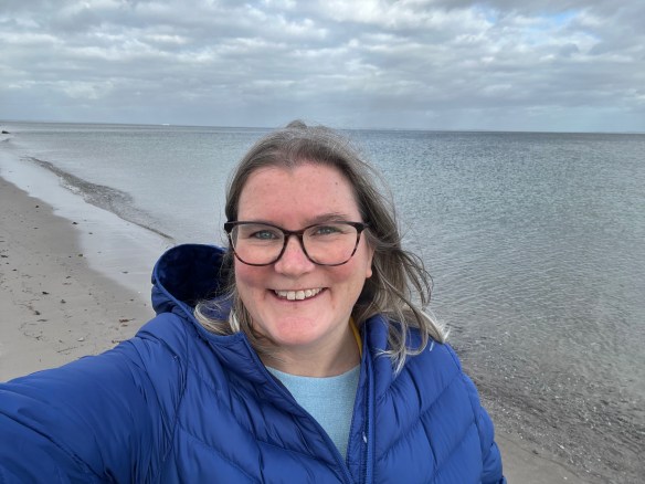 Smiley woman with glasses and blue coat standing by the sea